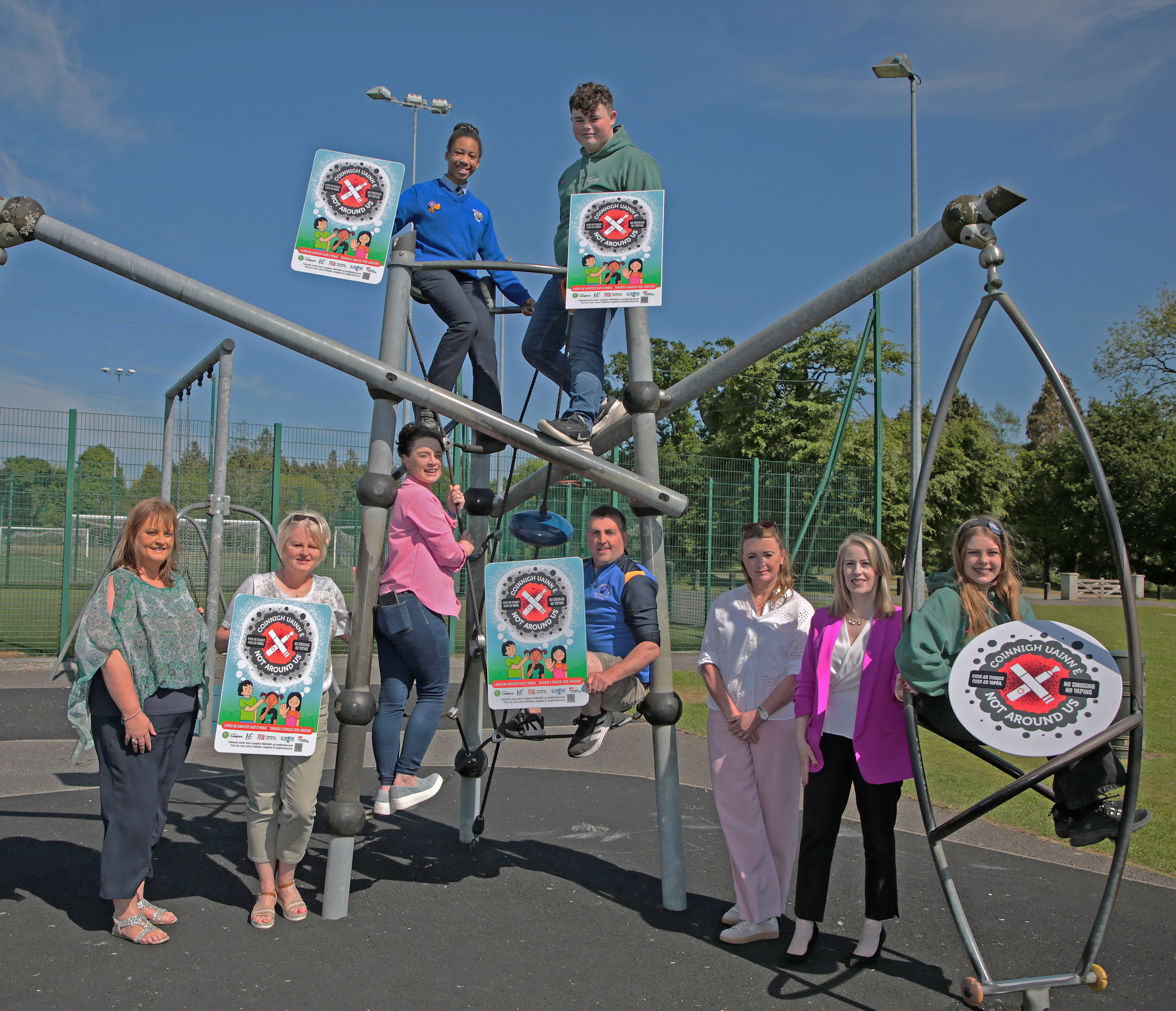 CB3B0149 Group of adults and young people with Not Around Us signage at a playground