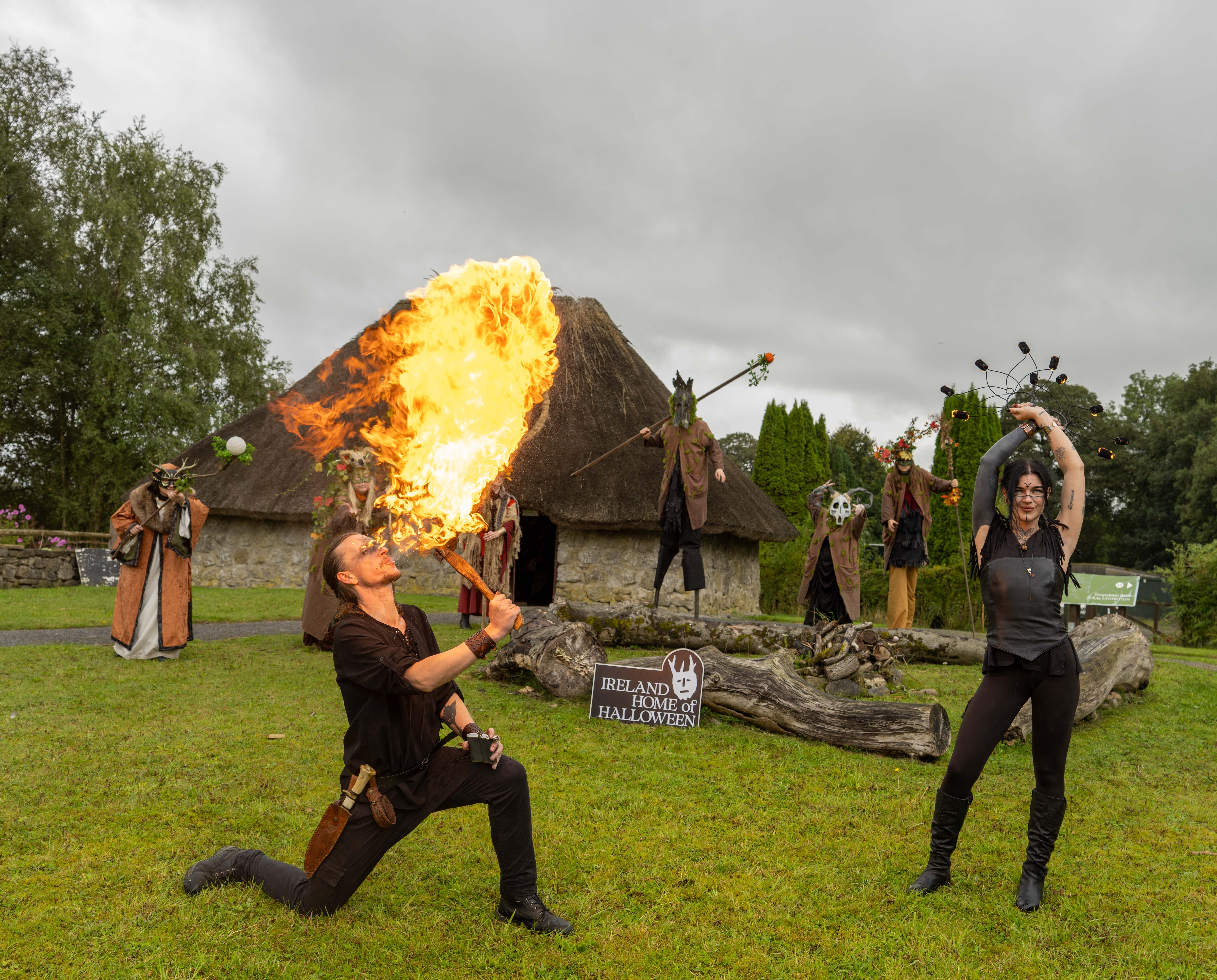 Person breathing fire in front of thatched cottage and people dressed in Celtic era costumes